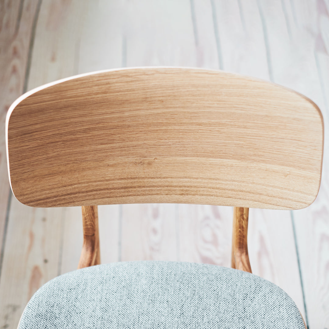 Light wooden chair back with natural grain, paired with soft blue upholstery for a modern, minimalist look.
