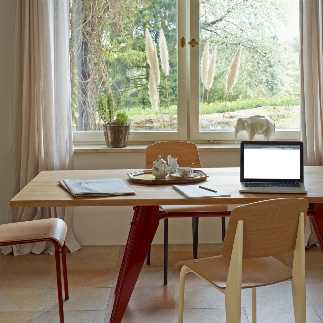 Modern wooden table with red legs, light beige chairs, and soft natural tones, creating a serene workspace atmosphere.