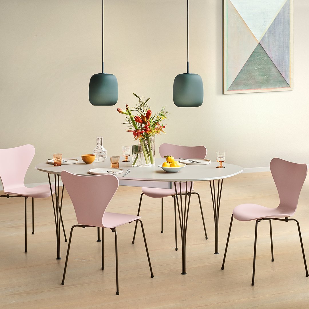 Modern dining table set featuring pastel pink chairs and sleek black legs, complemented by green pendant lights.