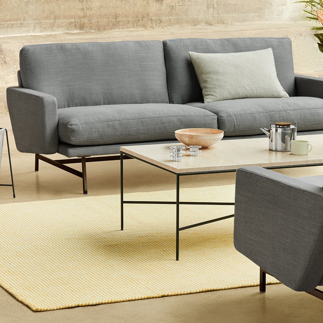 Gray modern sofa with a light green cushion, paired with a yellow rug and minimalist black metal table. Clean, contemporary design.