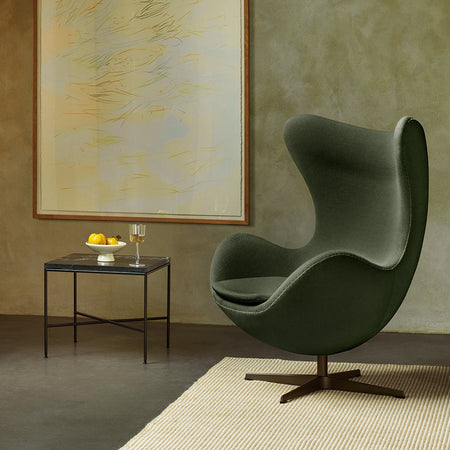 Green upholstered egg chair with smooth curves, paired with a sleek black side table. Patterned beige rug adds texture.