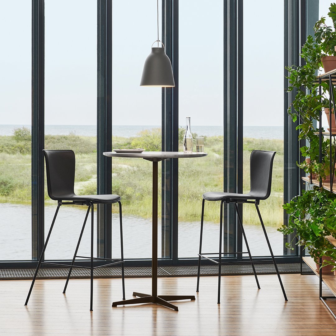 Modern black bar stools and table with a sleek design against a backdrop of large windows and natural greenery.
