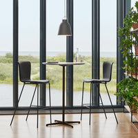Modern black bar stools and table with a sleek design against a backdrop of large windows and natural greenery.