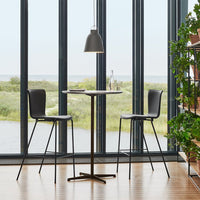 Textured black bar stools beside a sleek round table, set against large windows showcasing a green landscape.