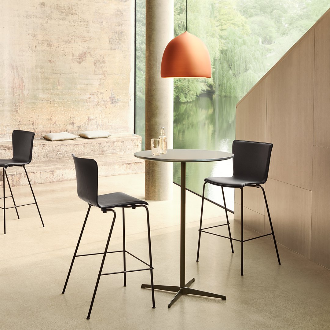 Modern black bar stools with sleek design beside a round table, accented by a warm orange pendant light. Neutral tones in the setting.