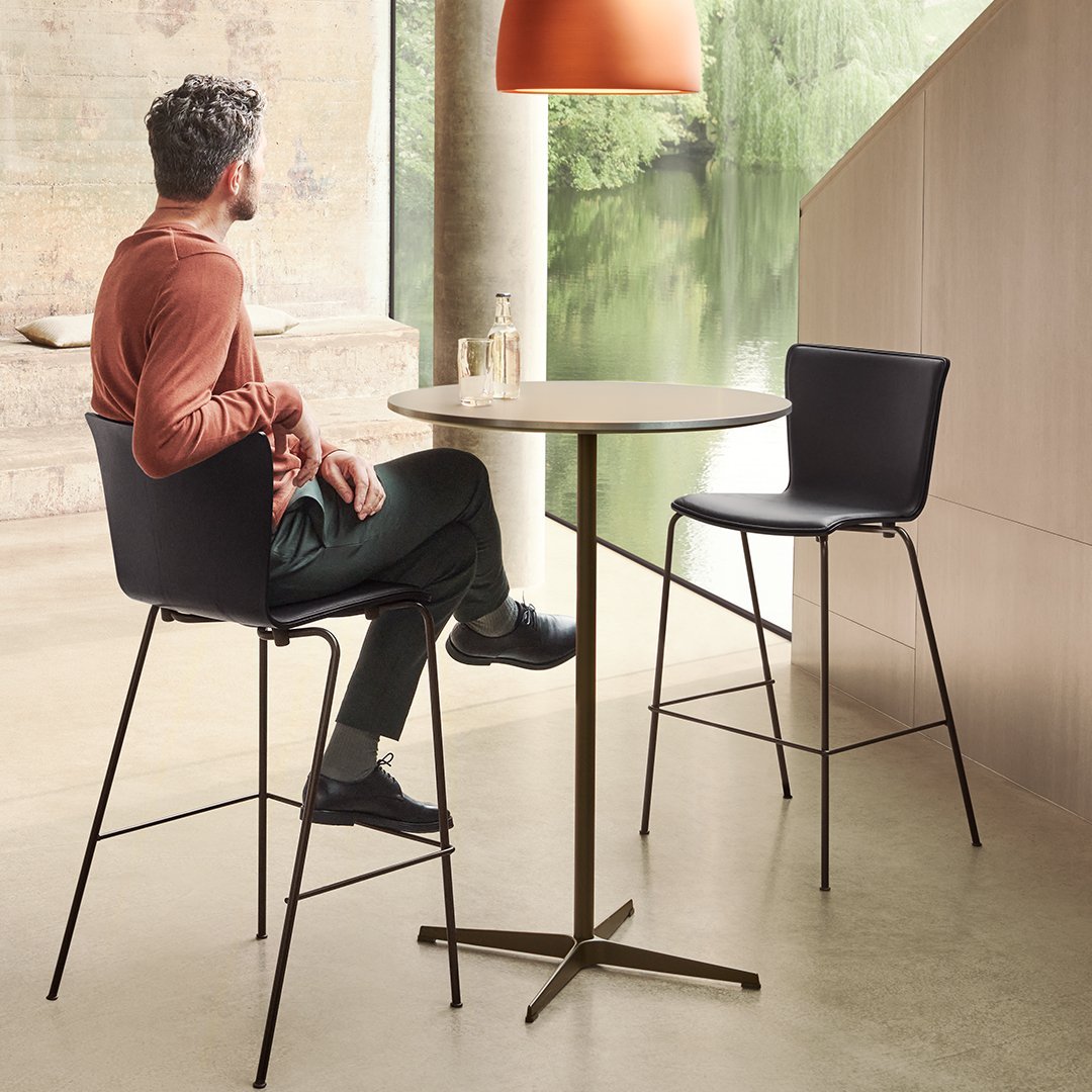 Modern black chairs and a light wood table against a neutral backdrop with earthy tones and a soft orange lamp.