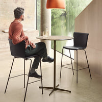Modern black chairs and a light wood table against a neutral backdrop with earthy tones and a soft orange lamp.