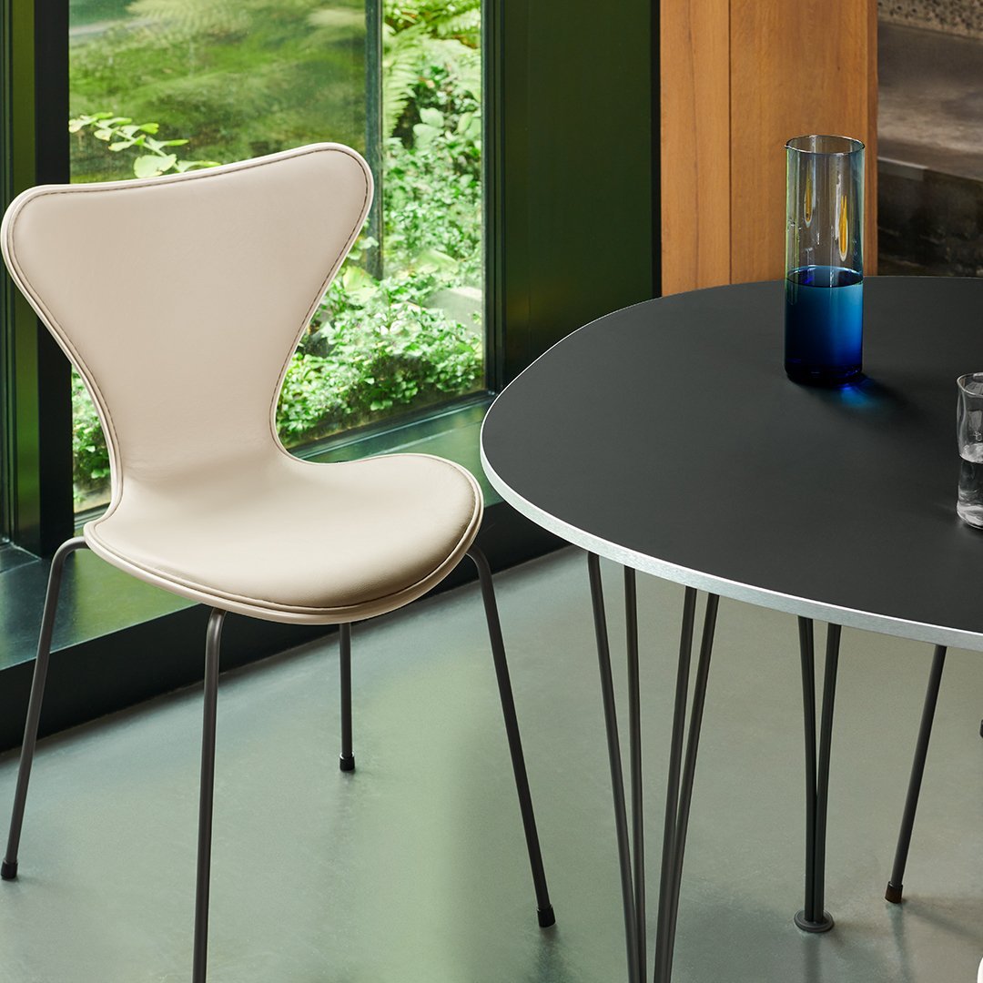Beige chair with a unique butterfly shape beside a sleek black round table, accented by a blue glass vase and clear water glass.