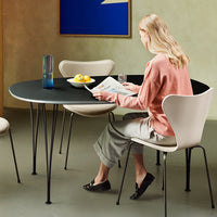 Modern round black table with minimalist design, paired with cream-colored chairs in a soft green setting.