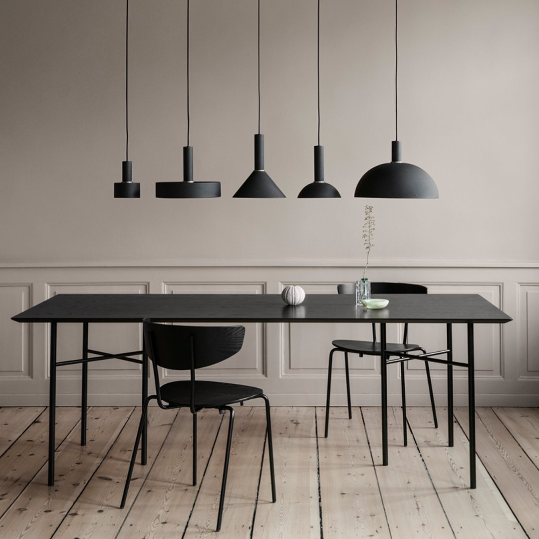 Sleek black dining table and chairs under modern black pendant lights, set against a soft neutral wall. Minimalist design.