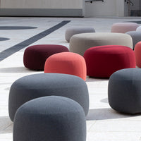 Colorful poufs in shades of gray, red, and pink, featuring round, soft shapes against a modern outdoor setting.