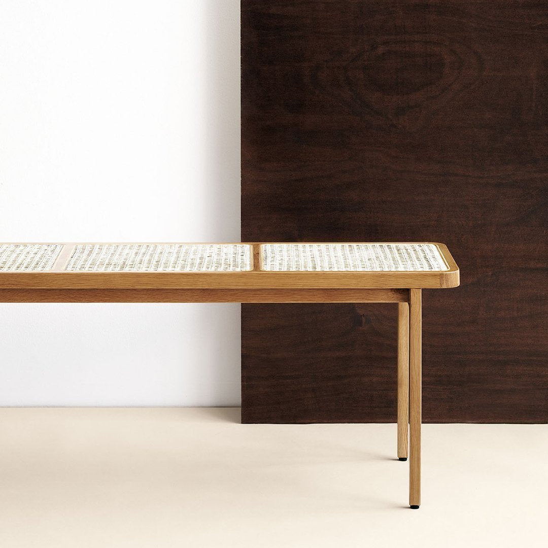 Light wood bench with a textured cream pattern on the top, set against a dark brown wall. Minimalist design.