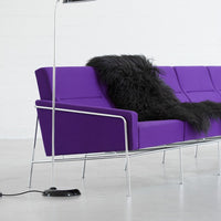 Vibrant purple sofa with sleek chrome legs, accented by a textured black fur throw, perfect for modern decor.