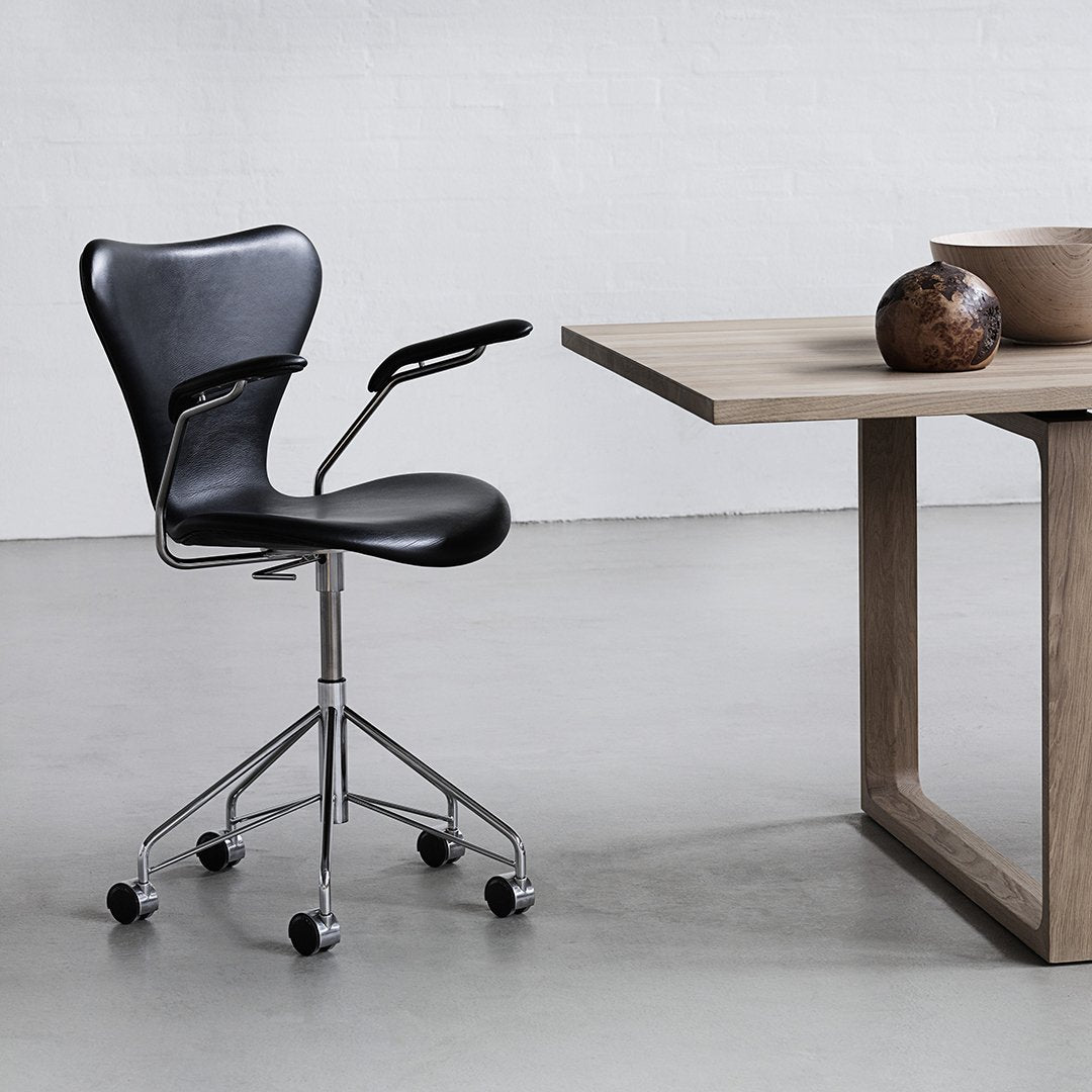 Black ergonomic chair with chrome base, paired with a wooden table, creating a sleek modern design.