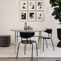 Minimalist round table with natural wood finish, black chairs, and a neutral rug, accented by framed art on the wall.
