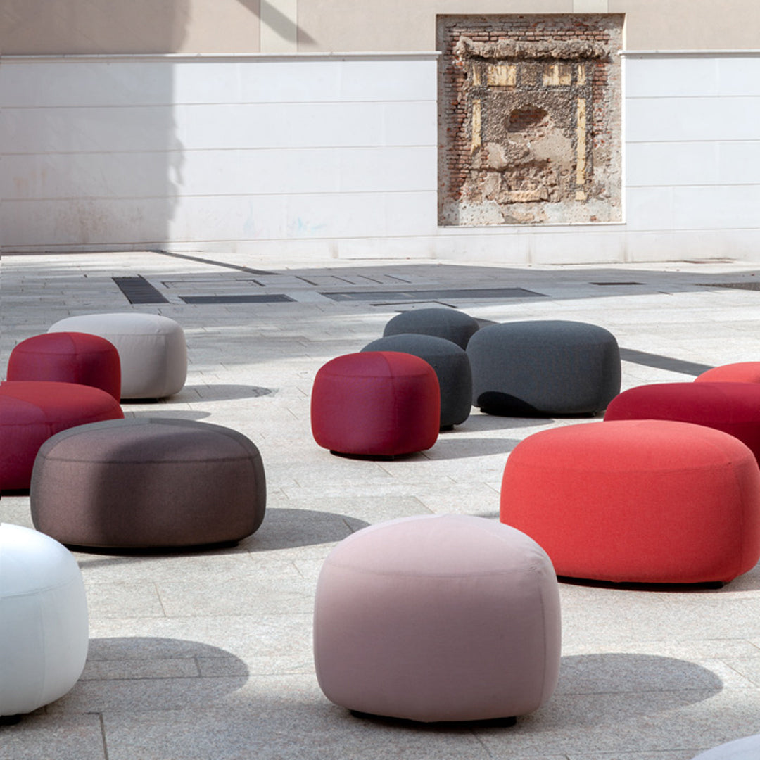 Colorful round poufs in shades of red, gray, white, and brown, featuring a soft, smooth texture.