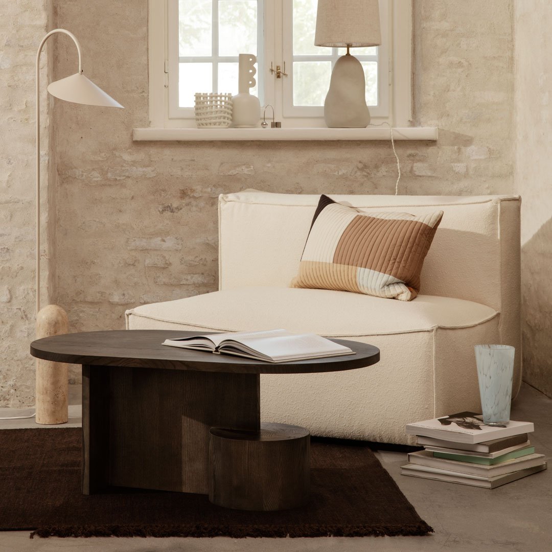 Beige couch with geometric brown and cream cushions, dark wood coffee table, and neutral decor in a minimalist room.