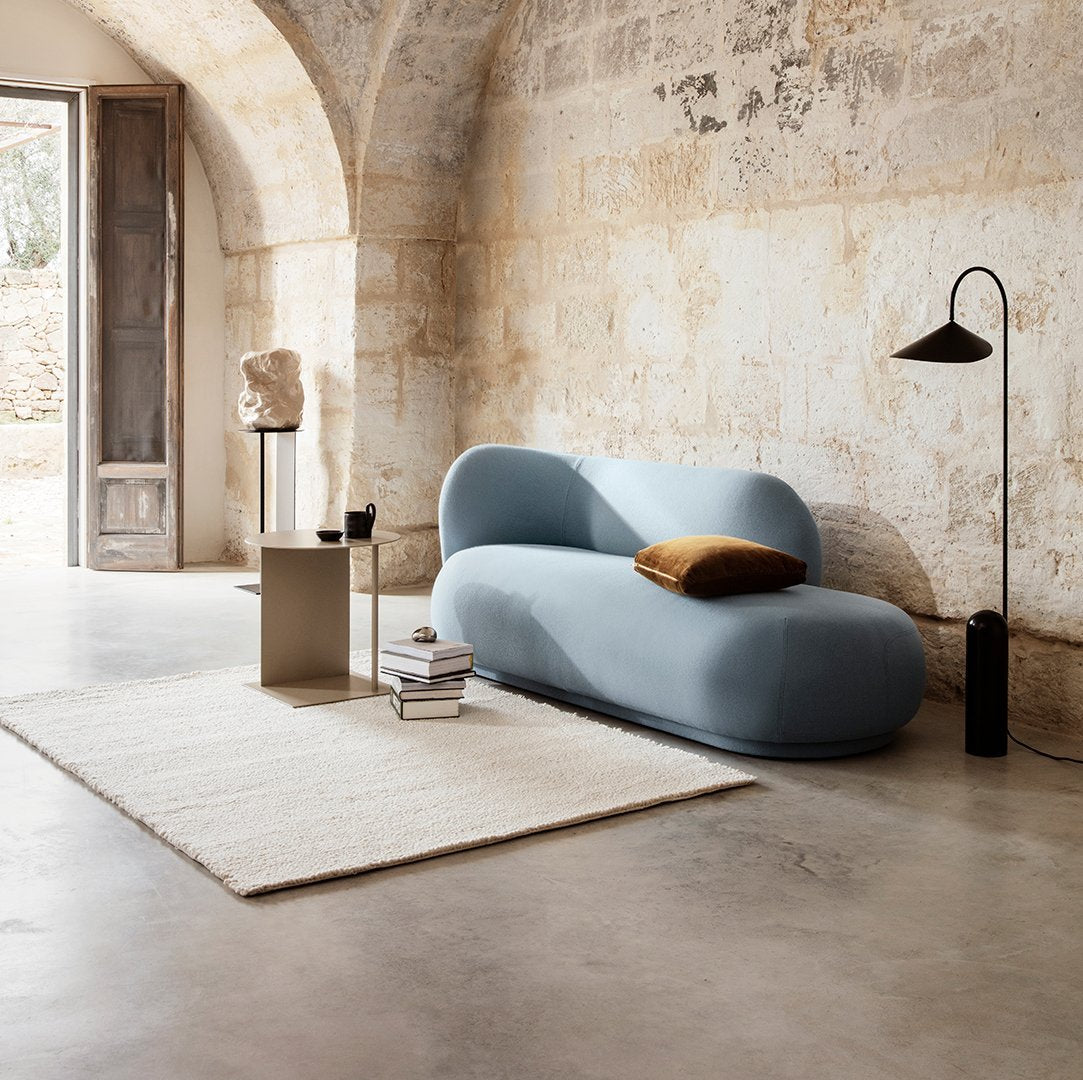 Soft blue curved sofa with a cozy brown cushion, paired with a neutral rug and minimalistic decor in a warm-toned setting.