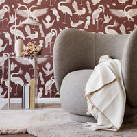 "Brown wallpaper with white flamingo and bird patterns, complemented by a gray chair and neutral textiles."