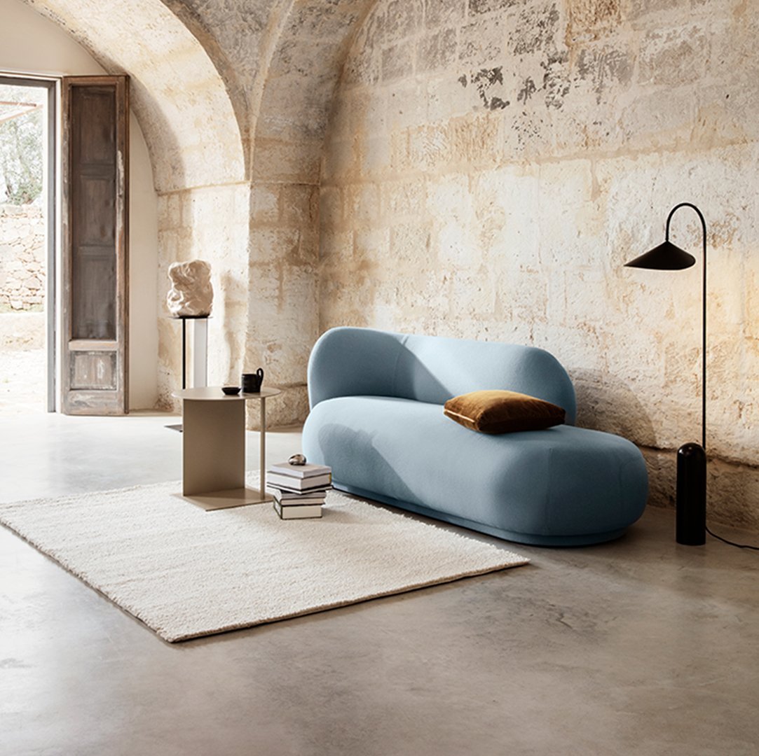 Curved blue sofa with a smooth texture, paired with a neutral rug and warm-toned accent pillow in a stylish setting.