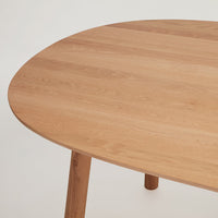 Light oak round table with smooth wood grain and natural finish, showcasing a minimalist design aesthetic.