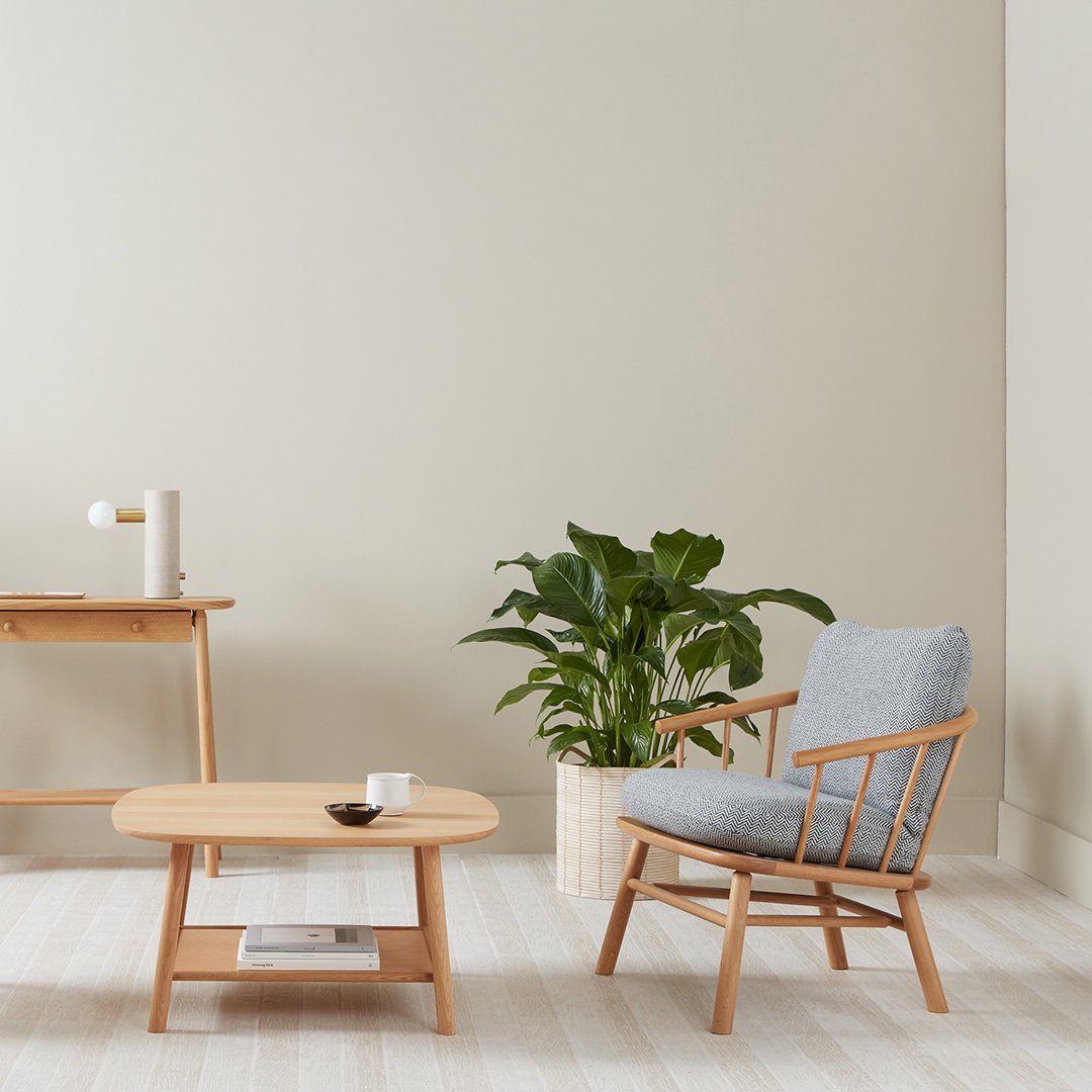 Light gray upholstered chair with a wooden frame, paired with a round wooden coffee table and a green indoor plant.