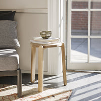 Light wood side table with a smooth finish, stacked books, and a patterned bowl, set against a bright, sunny room.