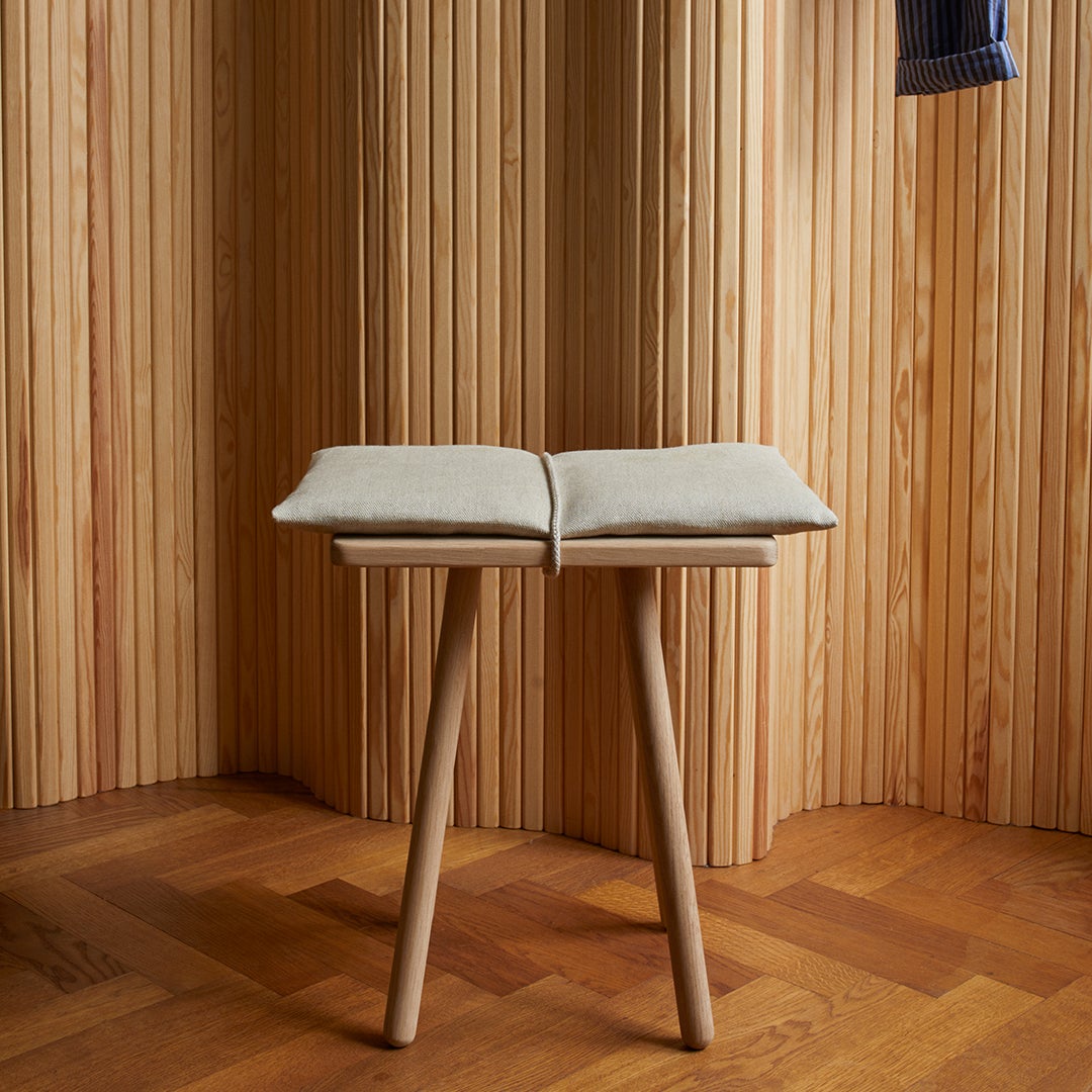 Beige cushion on light wooden stool with minimalist design and natural wood grain backdrop. Elegant and modern aesthetic.
