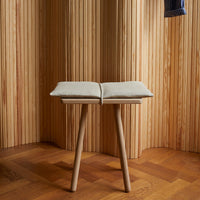 Beige cushion on light wooden stool with minimalist design and natural wood grain backdrop. Elegant and modern aesthetic.
