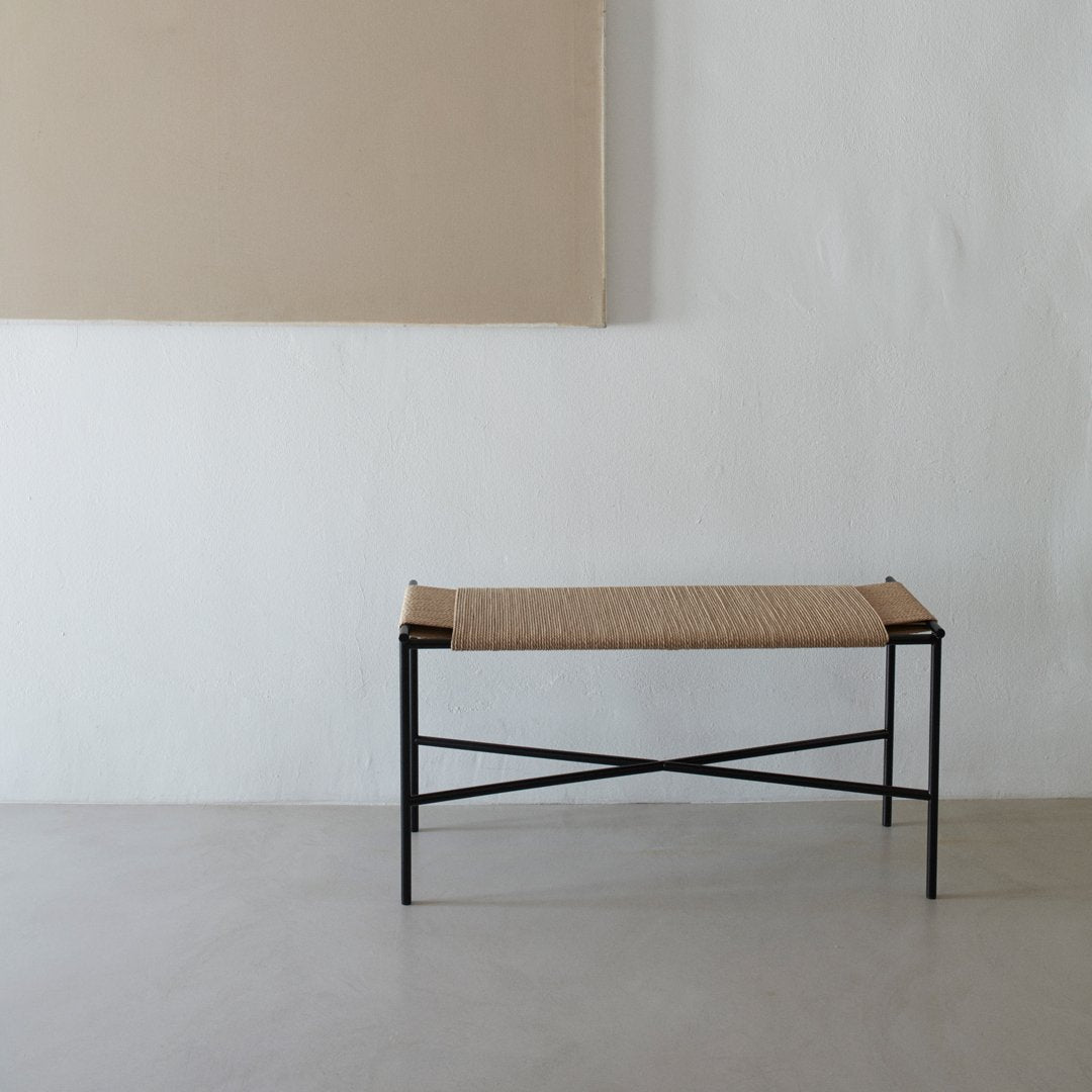 Natural woven pattern with a beige seat and black metal frame; minimalist design against a neutral backdrop.