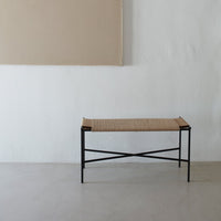 Natural woven pattern with a beige seat and black metal frame; minimalist design against a neutral backdrop.