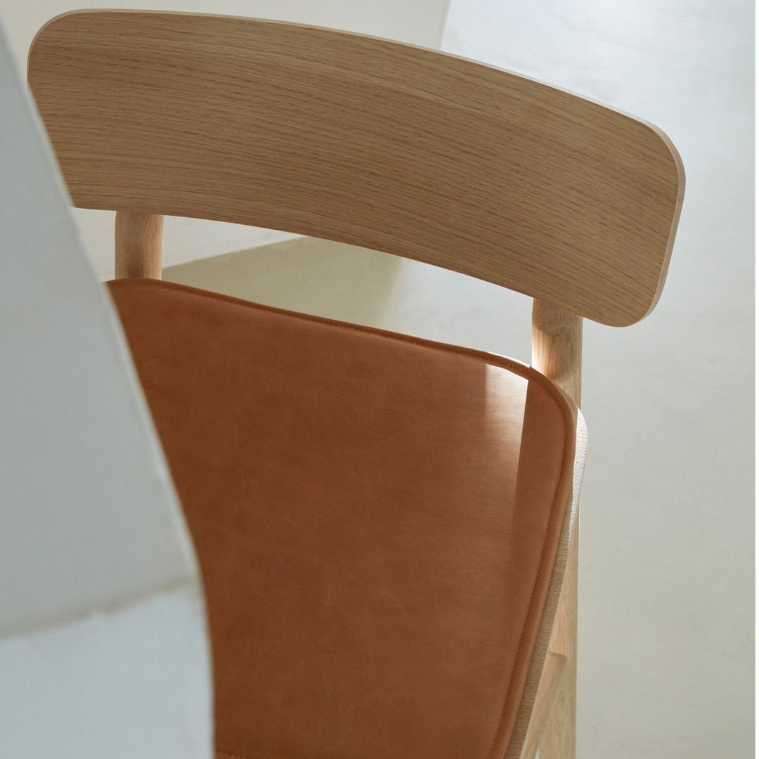 Wooden chair with light natural grain and a rich brown leather seat cushion. Minimalist modern design.