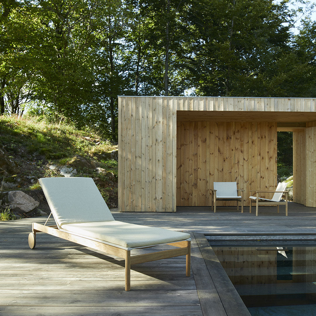 Light beige lounge chair with a minimalist design, complemented by natural wood tones and lush green surroundings.