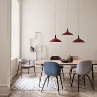 Modern dining room featuring warm red pendant lights, soft blue, gray, and muted pastel chairs against a neutral backdrop.