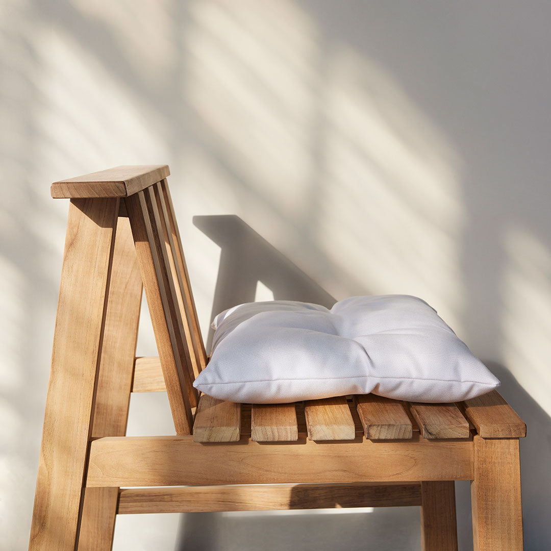 White cushion on a light wood chair, highlighting natural textures and soft shadows.