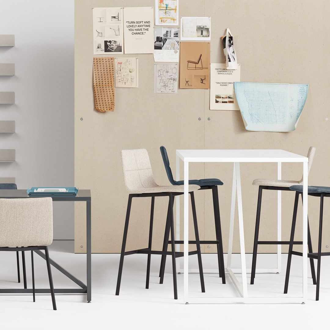Modern bar stools in neutral tones with blue and white accents against a light beige wall. Sleek, minimalist design.