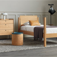 Stylish wooden bed frame with a warm oak finish, featuring neutral bedding and a patterned throw, set on a light rug.