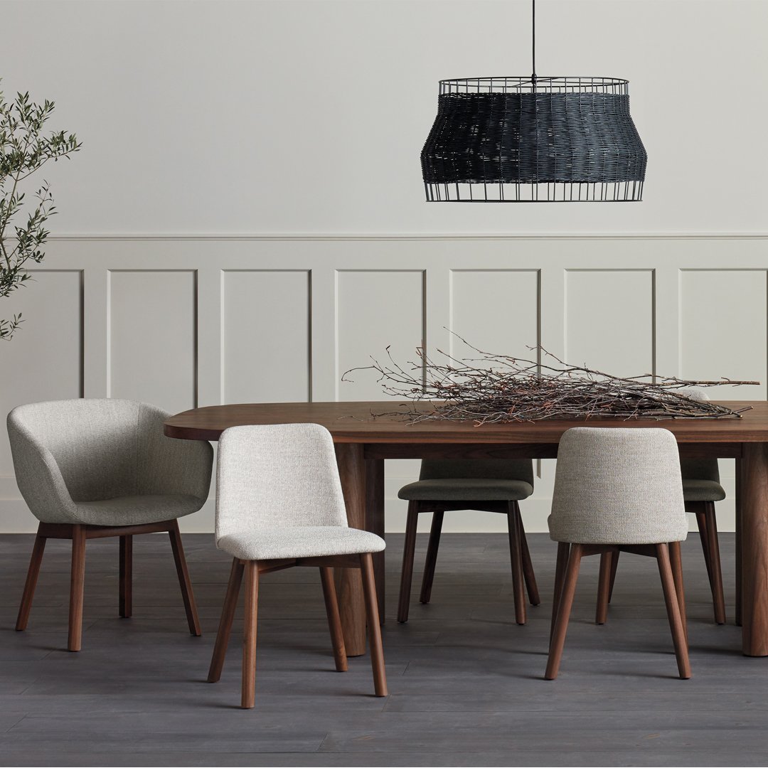 Modern dining set featuring neutral gray and beige chairs with warm wood tones and a textured black pendant light.