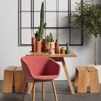 Modern setting featuring a pink chair, earthy tone vases in terracotta and muted colors, with greenery in a minimalist style.