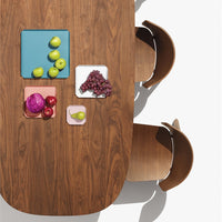 Wooden table with vibrant blue, pink, and white plates, featuring green apples, purple cabbage, and red grapes.