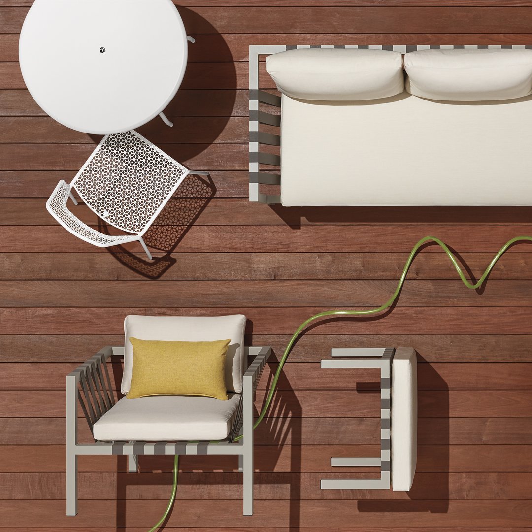 Modern outdoor furniture in neutral tones with a pop of yellow on a wooden deck with geometric patterns.