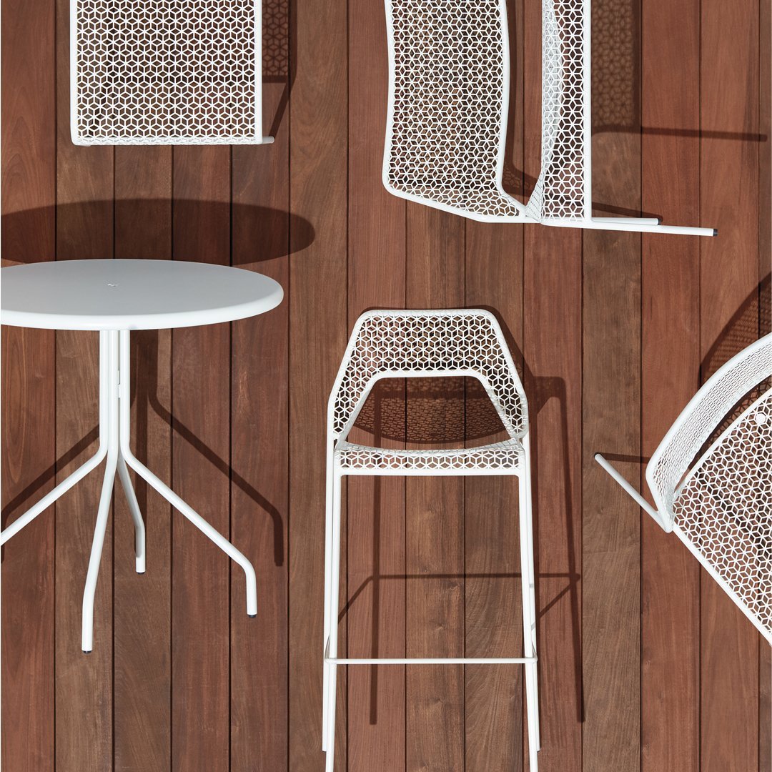 White lattice-patterned furniture on wooden floor, featuring a round table and bar stools. 
