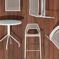 White lattice-patterned furniture on wooden floor, featuring a round table and bar stools. 