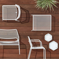 White patio furniture with a perforated pattern, set against a warm wood background and green plant accents.