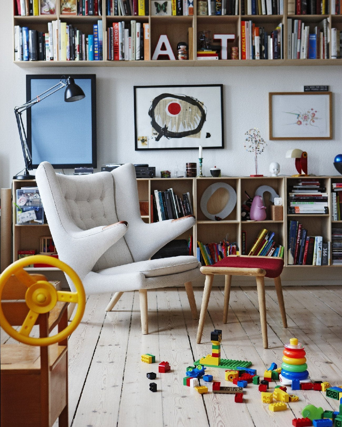 "White tufted armchair with wooden legs, surrounded by colorful books and toys on light wooden floor."