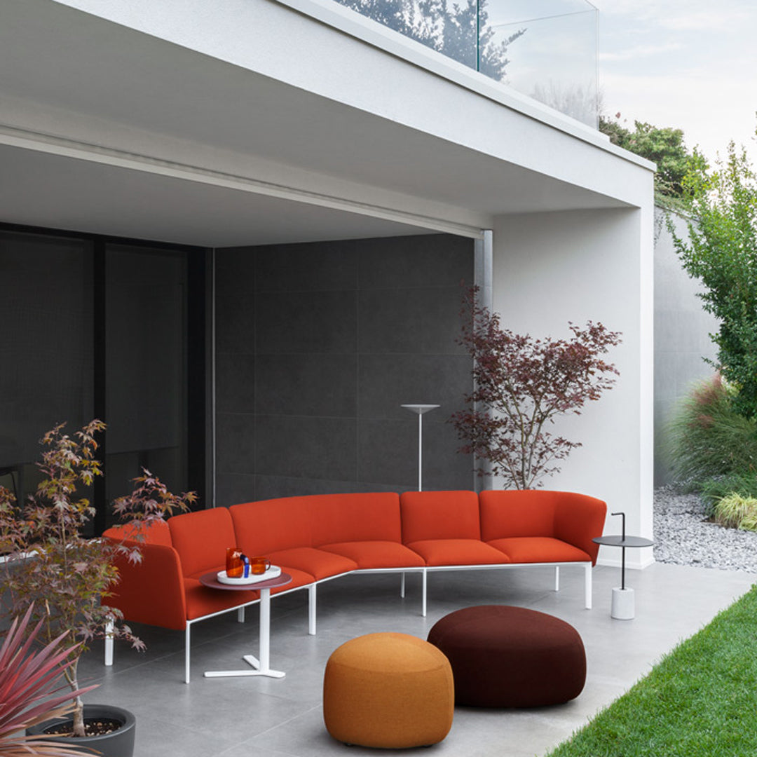 Modern curved sofa in vibrant orange upholstery, paired with round brown and orange poufs, set against a sleek gray backdrop.