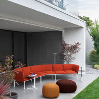 Modern curved sofa in vibrant orange upholstery, paired with round brown and orange poufs, set against a sleek gray backdrop.