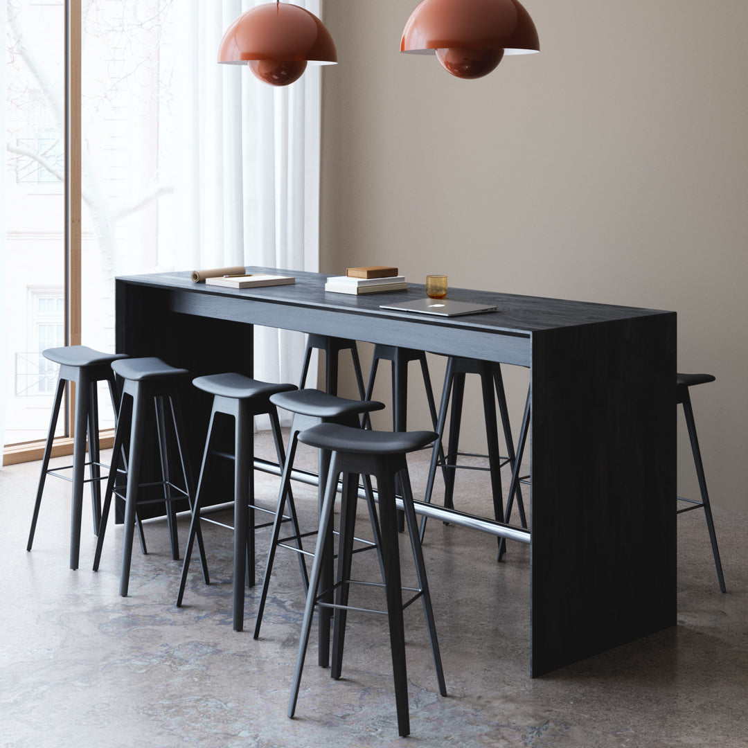 Sleek black bar table with high stools, complemented by warm amber pendant lights in a modern, airy setting.