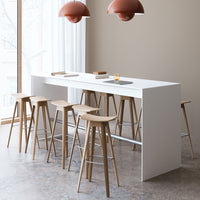 Minimalist white bar table with natural wood chairs, accentuated by warm, terracotta pendant lamps.