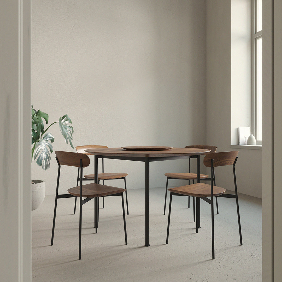 Modern round wooden table with black metal legs, complemented by four minimalist brown chairs, in a neutral-toned room.
